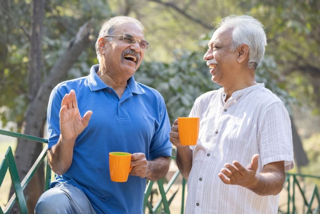 Two senior friends having fun raising a toast with coffee cups at park