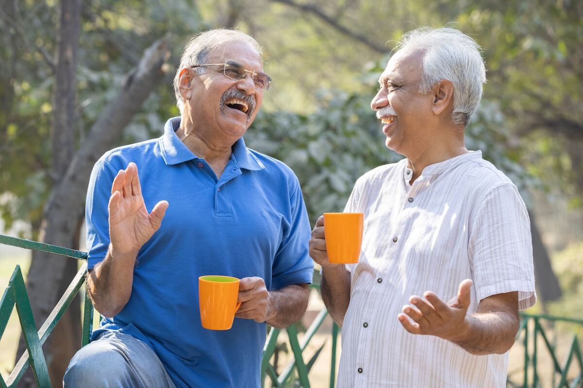 Two senior friends having fun raising a toast with coffee cups at park