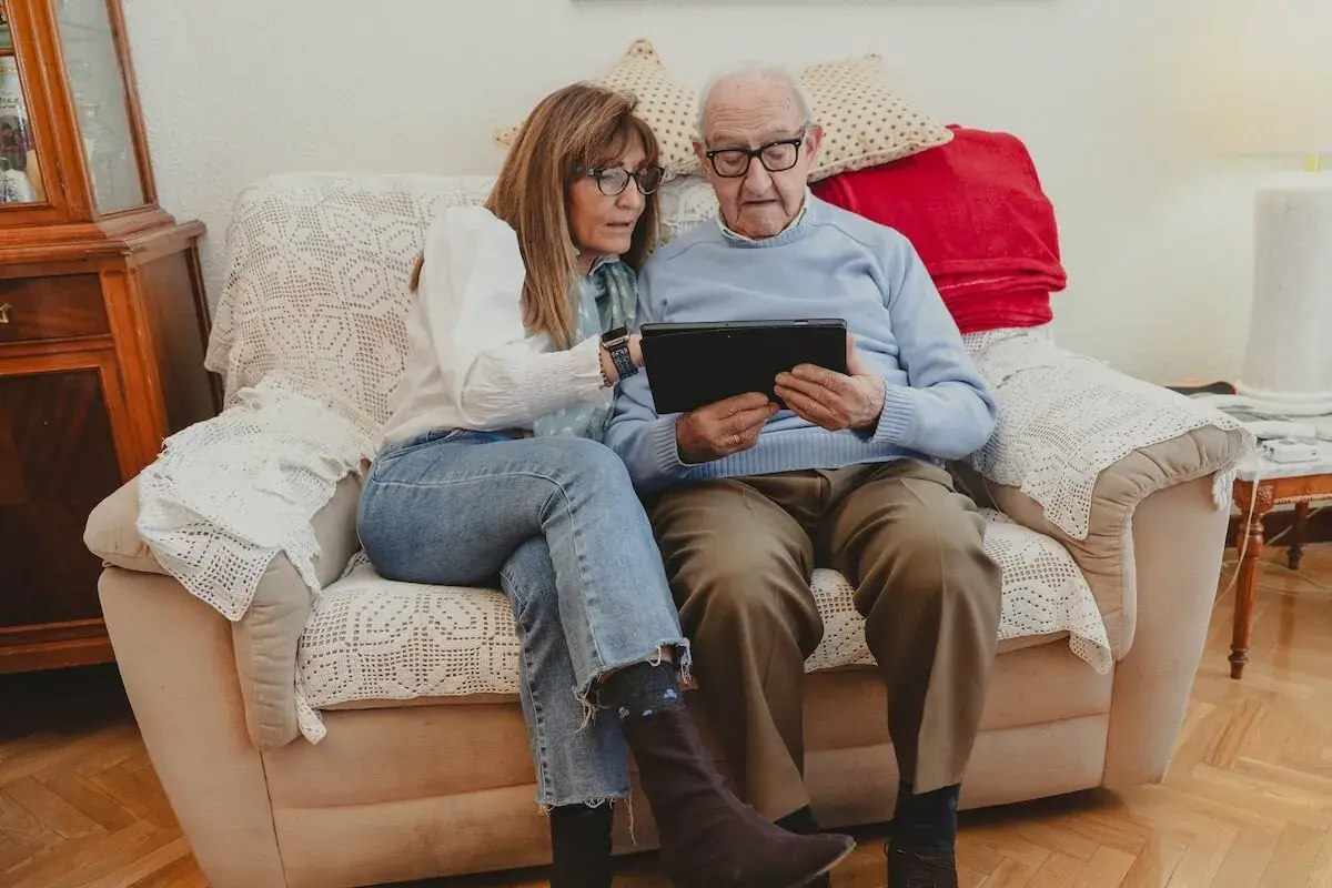 Daughter helping senior father navigate a tablet.