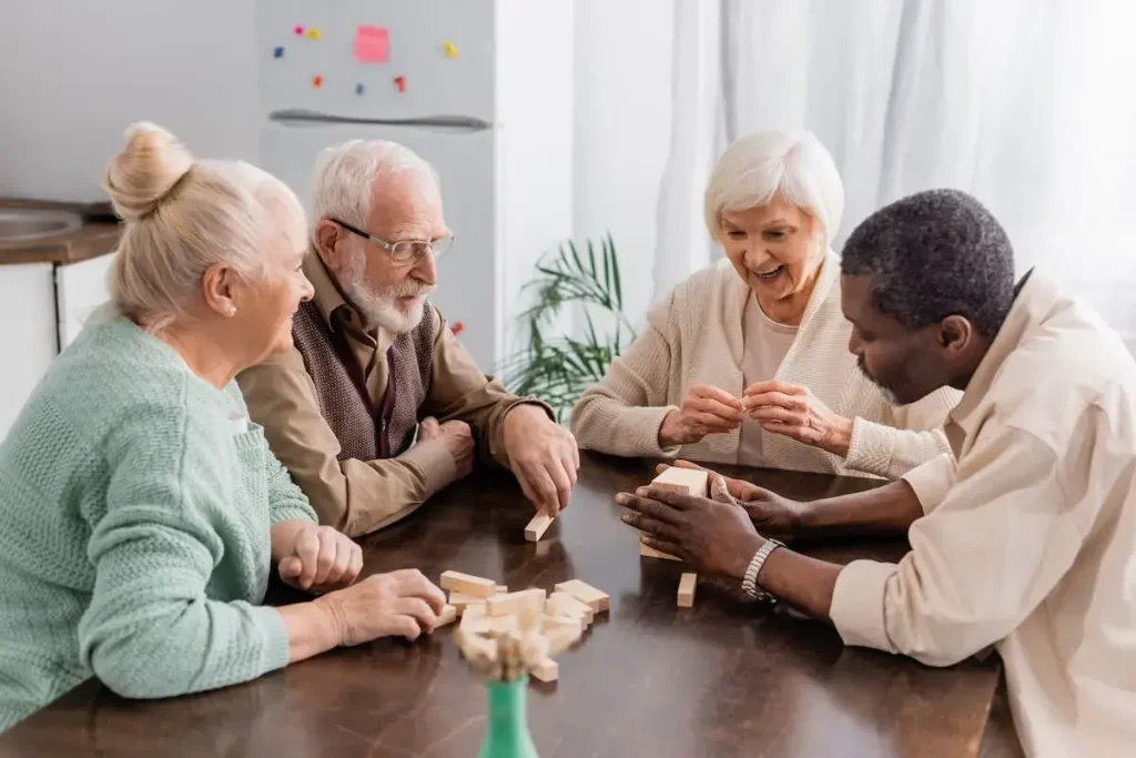 Excited senior woman smiling while playing tower wood blocks game with interracial friends