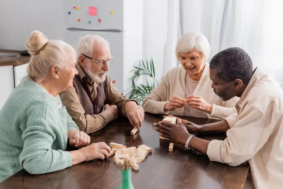 Excited senior woman smiling while playing tower wood blocks game with interracial friends