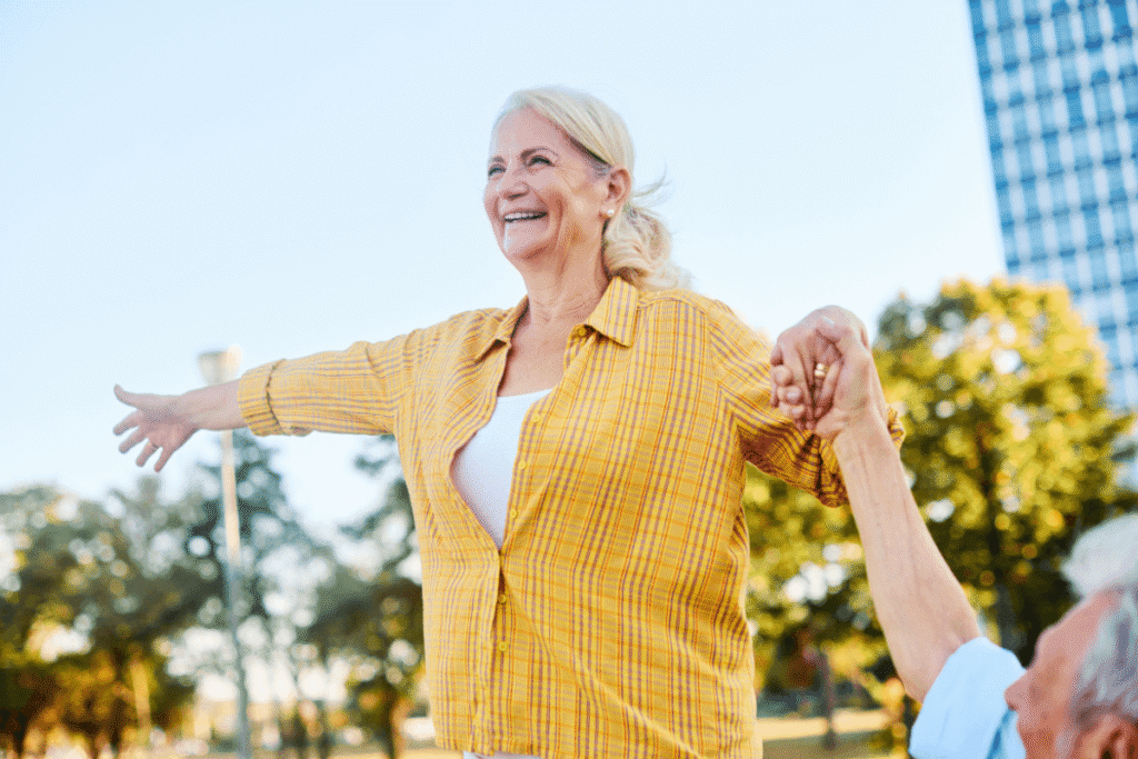 Happy senior mature couple having fun walking and balancing on a bench, bonding in a park outdoors.