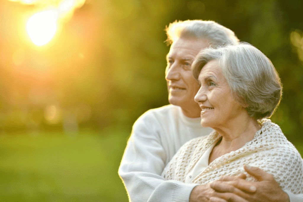An elderly couple sharing a joyful moment outdoors, surrounded by autumn leaves and bathed in the warm glow of a setting sun.